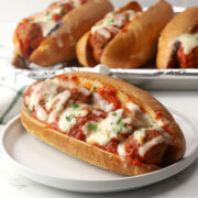 A meatball sub on a serving plate topped with melted cheese and chopped parsley.
