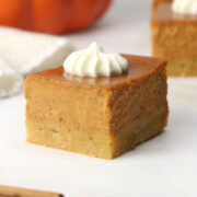 A square pumpkin pie bar in a countertop with a dollop of whipped cream on top.