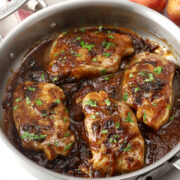 A saute pan filled with apple butter pork chops garnished with parsley.