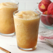 Two glasses filed with apple cider slushie with a bowl of apples.