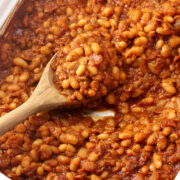 Baked beans in a casserole dish with a wooden spoon.