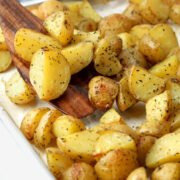 Herb roasted potatoes being scooped on a sheet pan.