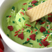 A layered vanilla cookie dipping into a bowl of grinch dip.