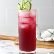 A glass of pomegranate spritzer with rosemary and lime garnish.