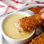 A chicken tender being dipped into honey mustard sauce.