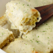 White chicken lasagna roll ups being scooped out of a dish.