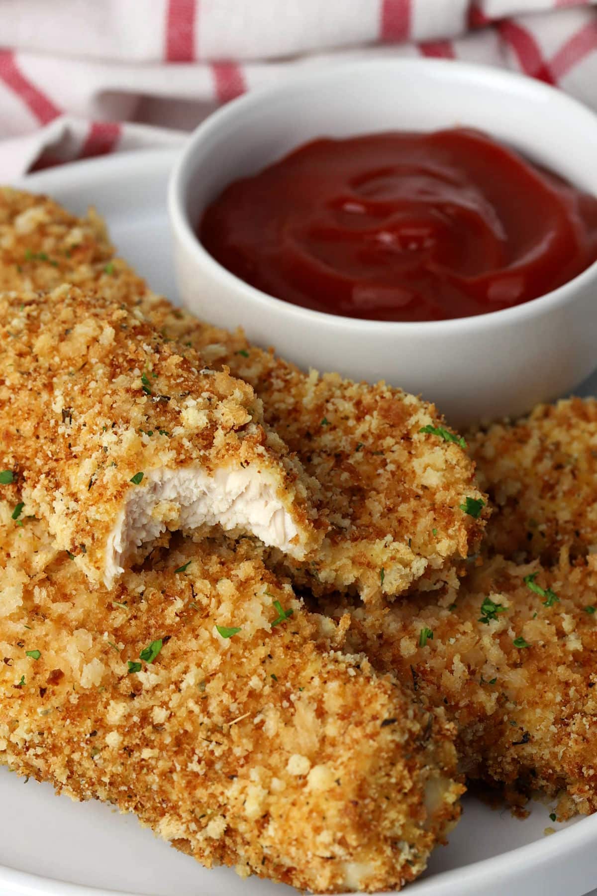 Close up of parmesan chicken tenders, one with a bite missing.