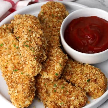 Plate of baked parmesan chicken tenders with a bowl of ketchup.
