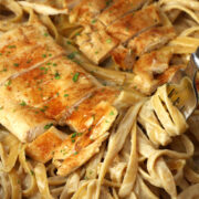 A fork twirling fettuccine alfredo in a sauté pan with Cajun chicken.