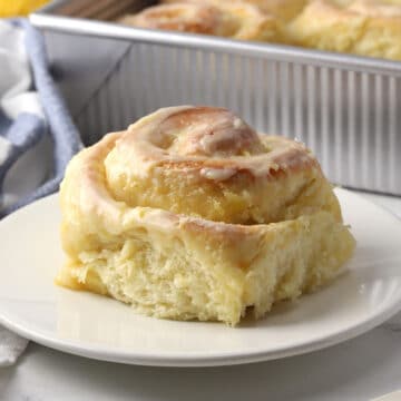 A lemon sweet roll on a plate with a pan in the background.