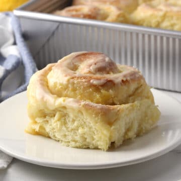 A lemon sweet roll on a plate with a pan in the background.