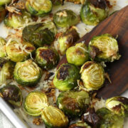 A wooden spatula scooping brussels sprouts off of a sheet pan.