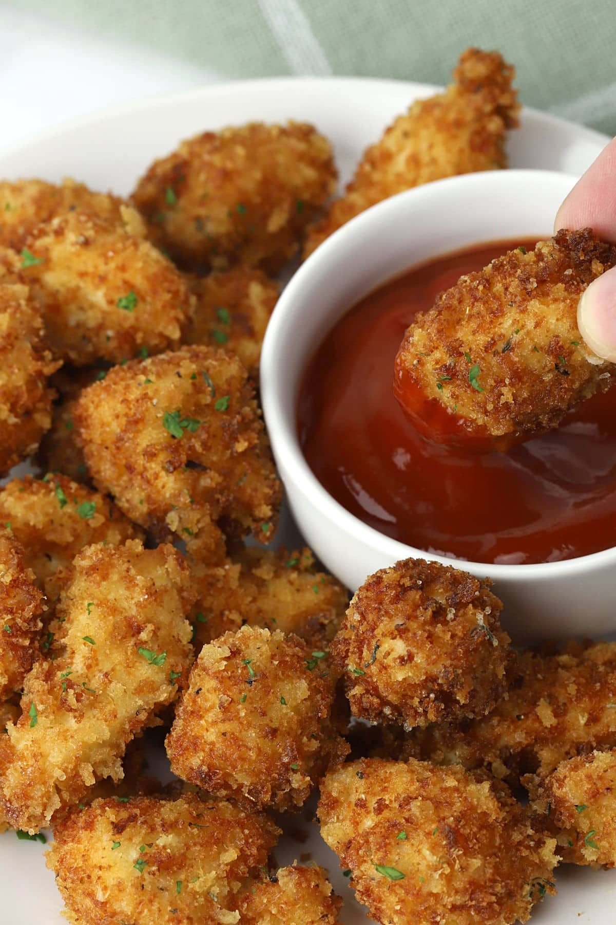 A parmesan chicken nugget being dipped into a bowl of sauce.