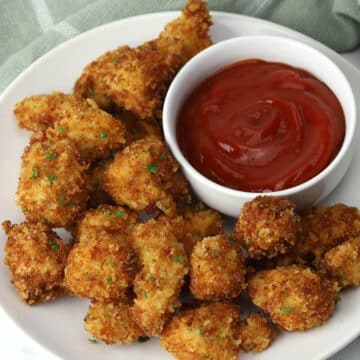 A plate of parmesan chicken nuggets with a bowl of dipping sauce.