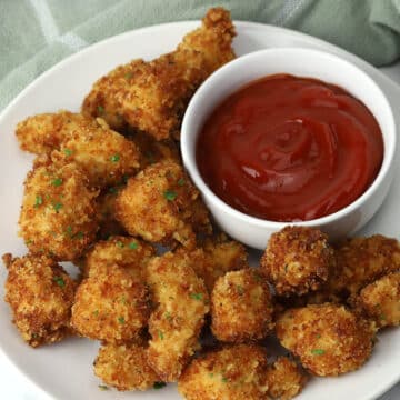 A plate of parmesan chicken nuggets with a bowl of dipping sauce.