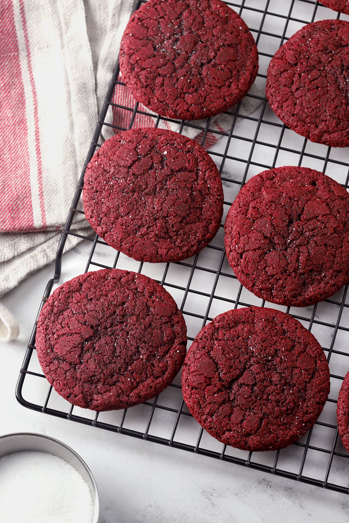 Red velvet sugar cookies spread on a cooling rack.