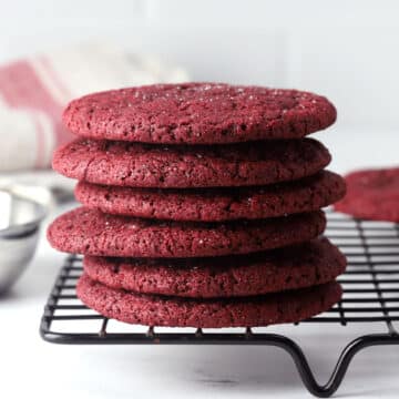 Red velvet sugar cookies stacked on a cooling rack.