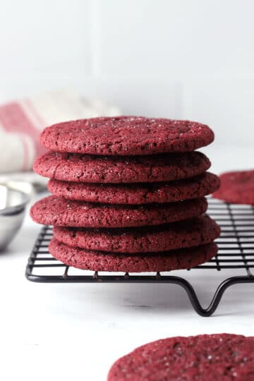 Red velvet sugar cookies stacked on a cooling rack.
