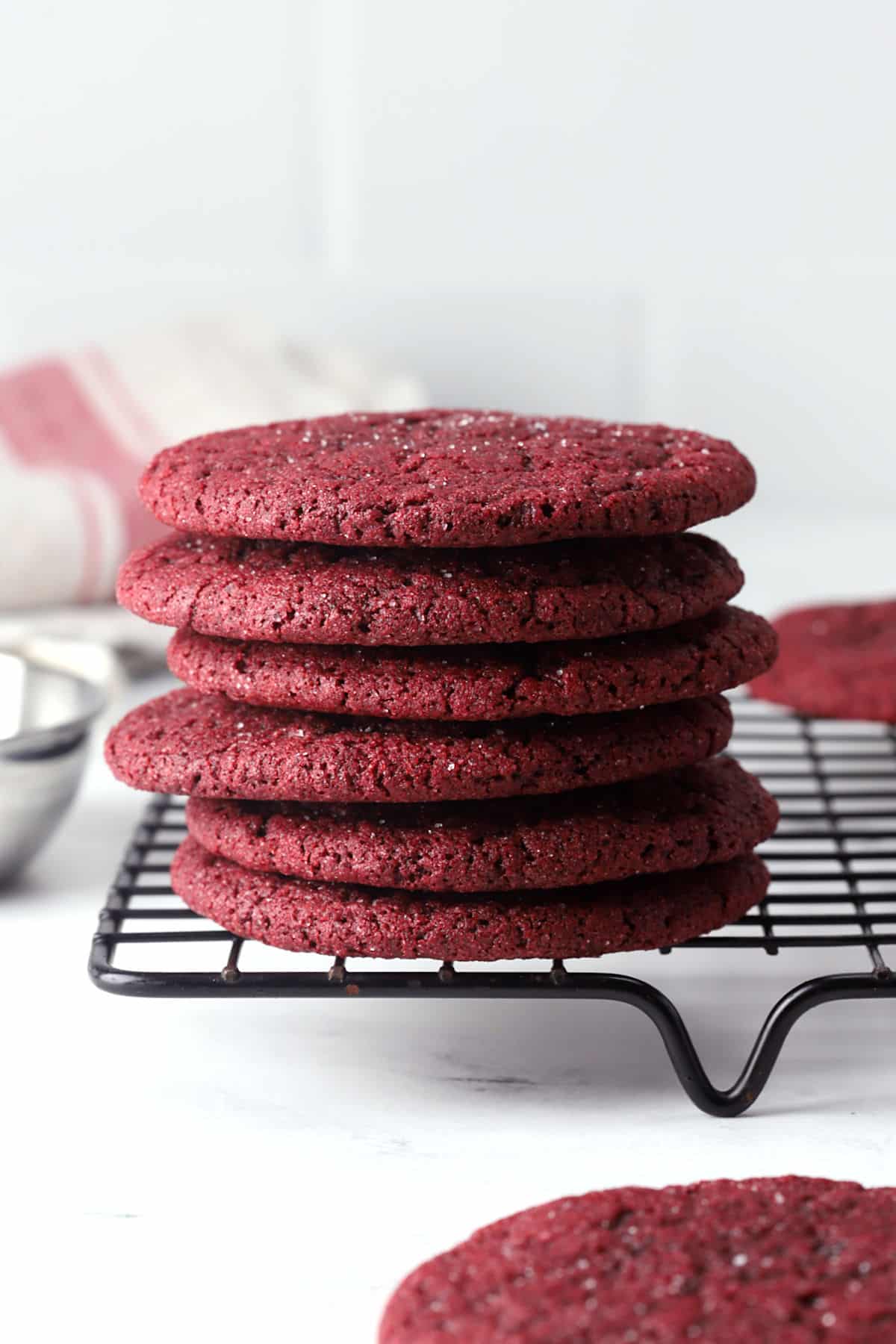 Red velvet sugar cookies stacked on a cooling rack.