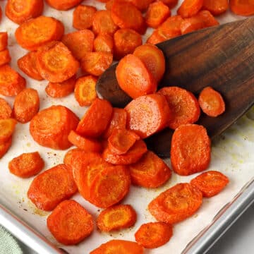 Scooping roasted carrots with a wooden spatula.