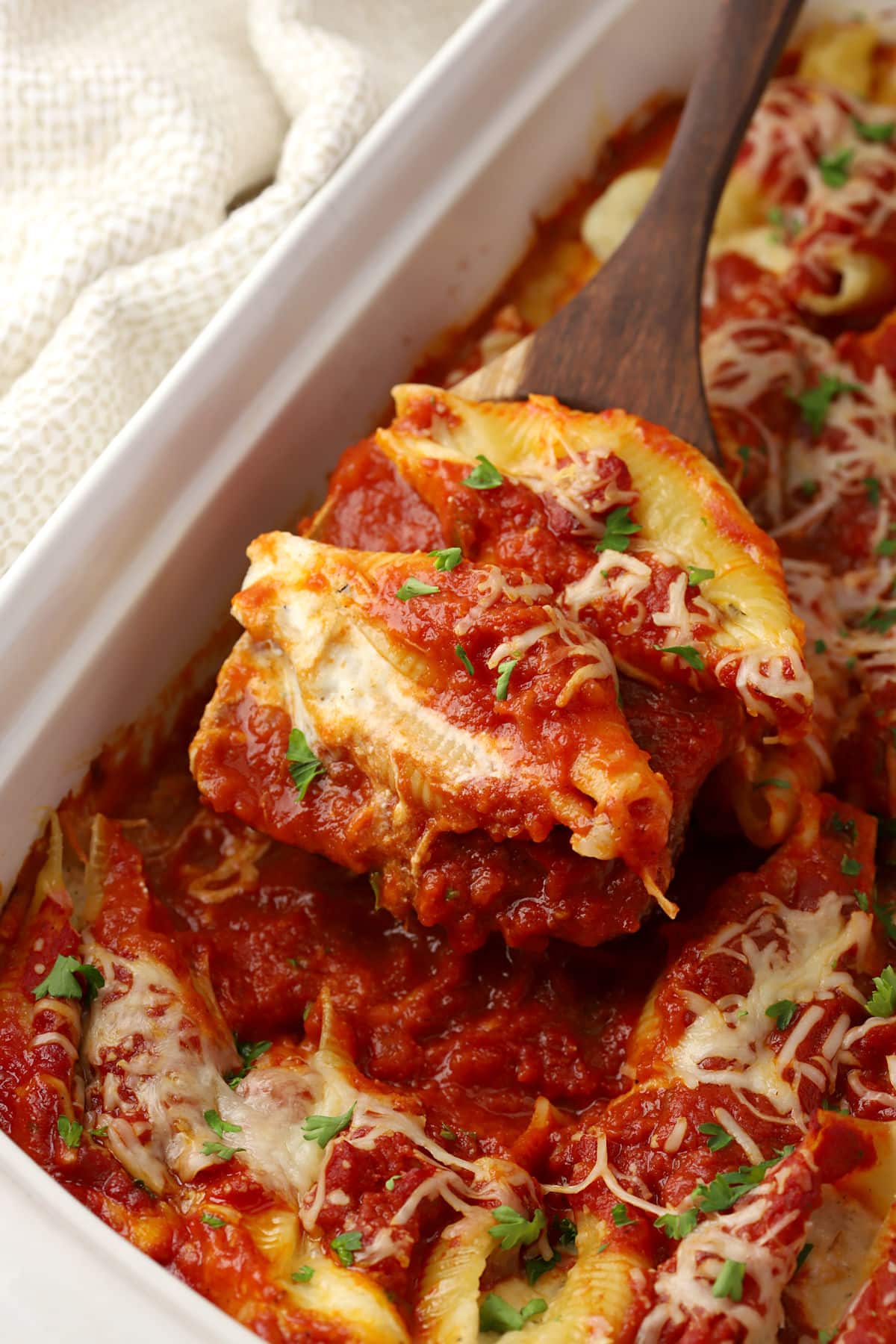Scooping cheese stuffed shells from a casserole dish.