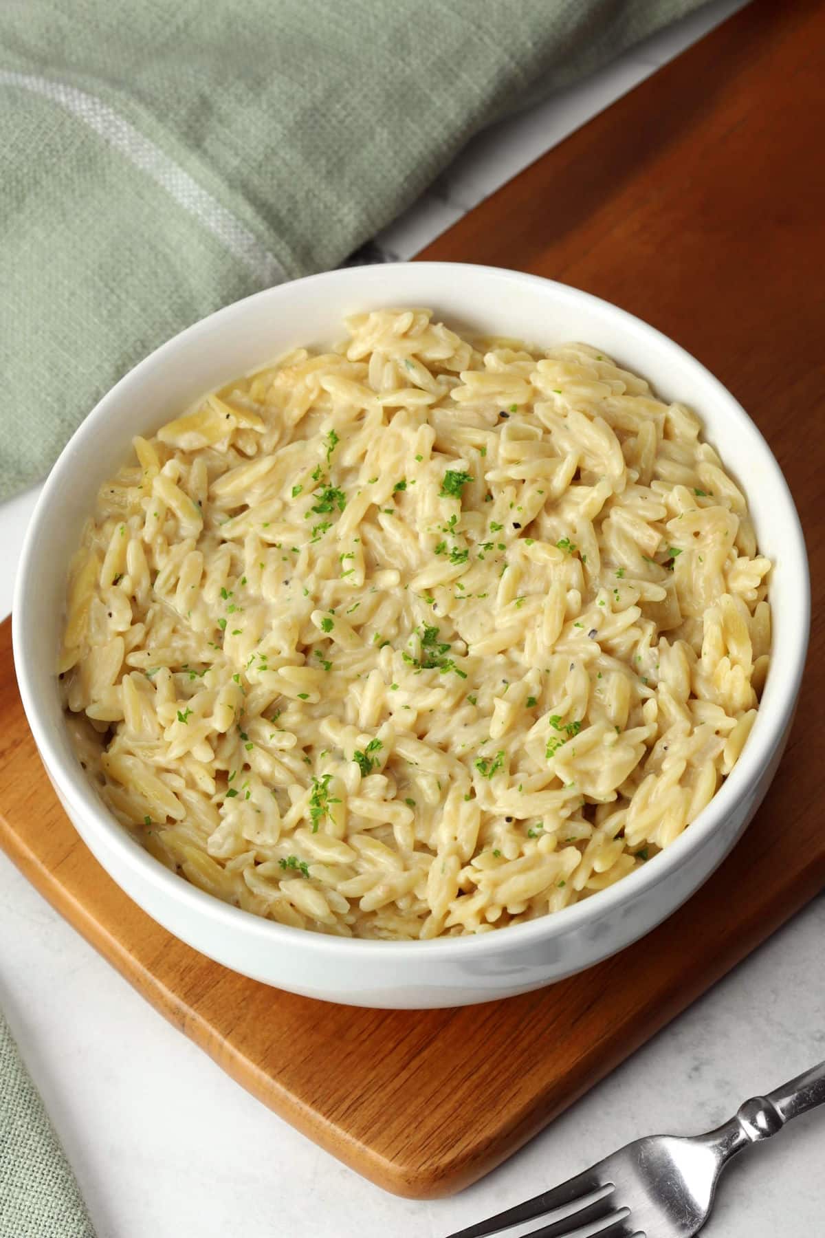 A bowl of orzo on a wooden cutting board.