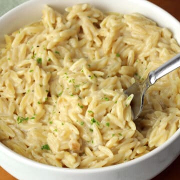A bowl of cheesy orzo with a metal fork.