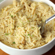A bowl of cheesy orzo with a metal fork.