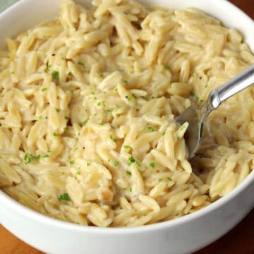 A bowl of cheesy orzo with a metal fork.