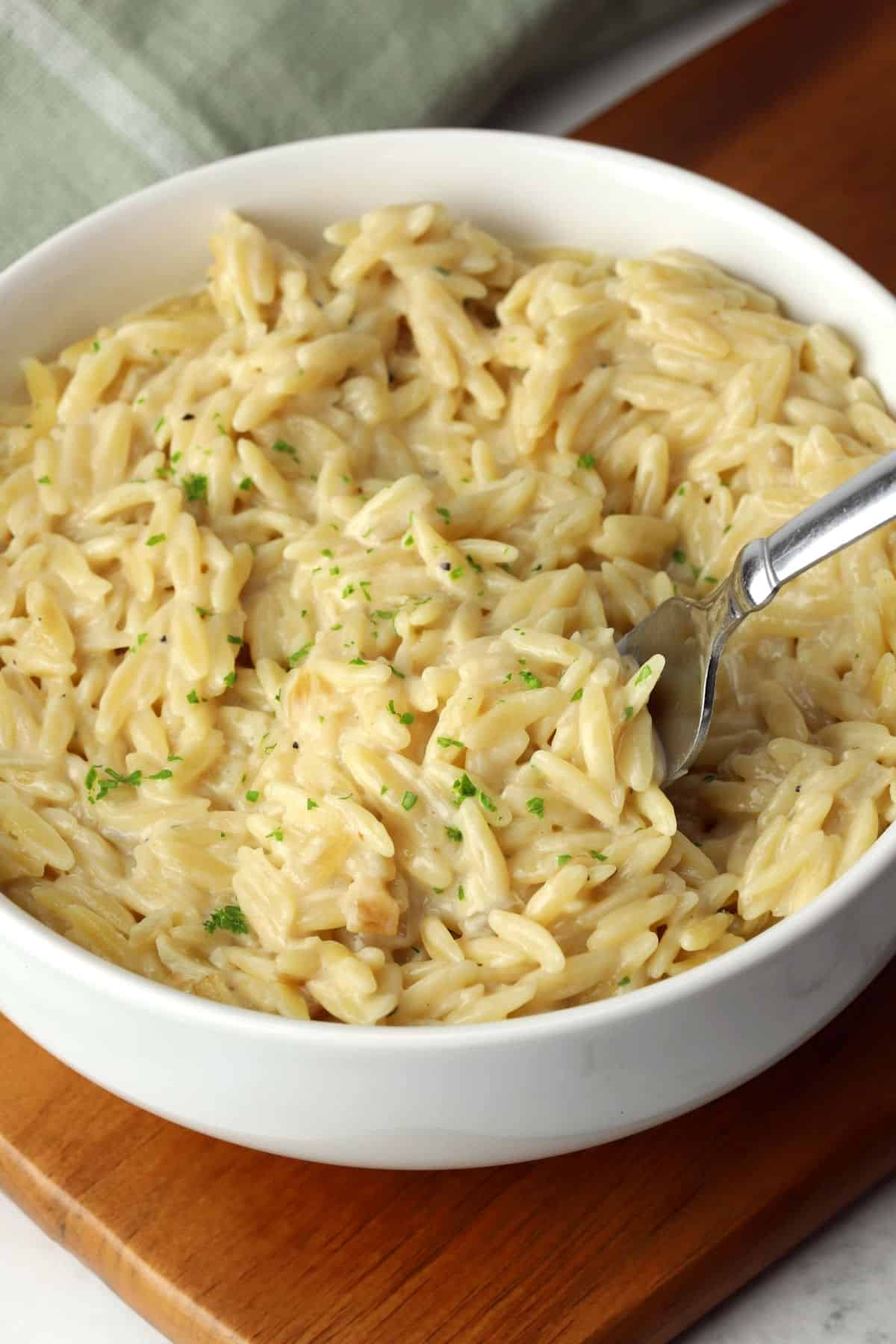 A bowl of cheesy orzo with a metal fork.