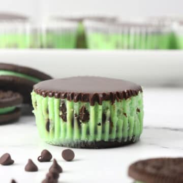 A mint chocolate chip mini cheesecake unwrapped on a cutting board.
