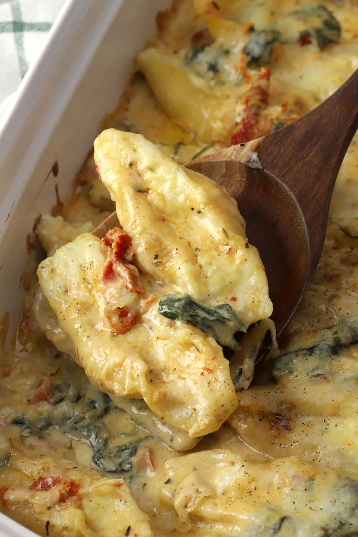 Stuffed shells being scooped out of a cream sauce.