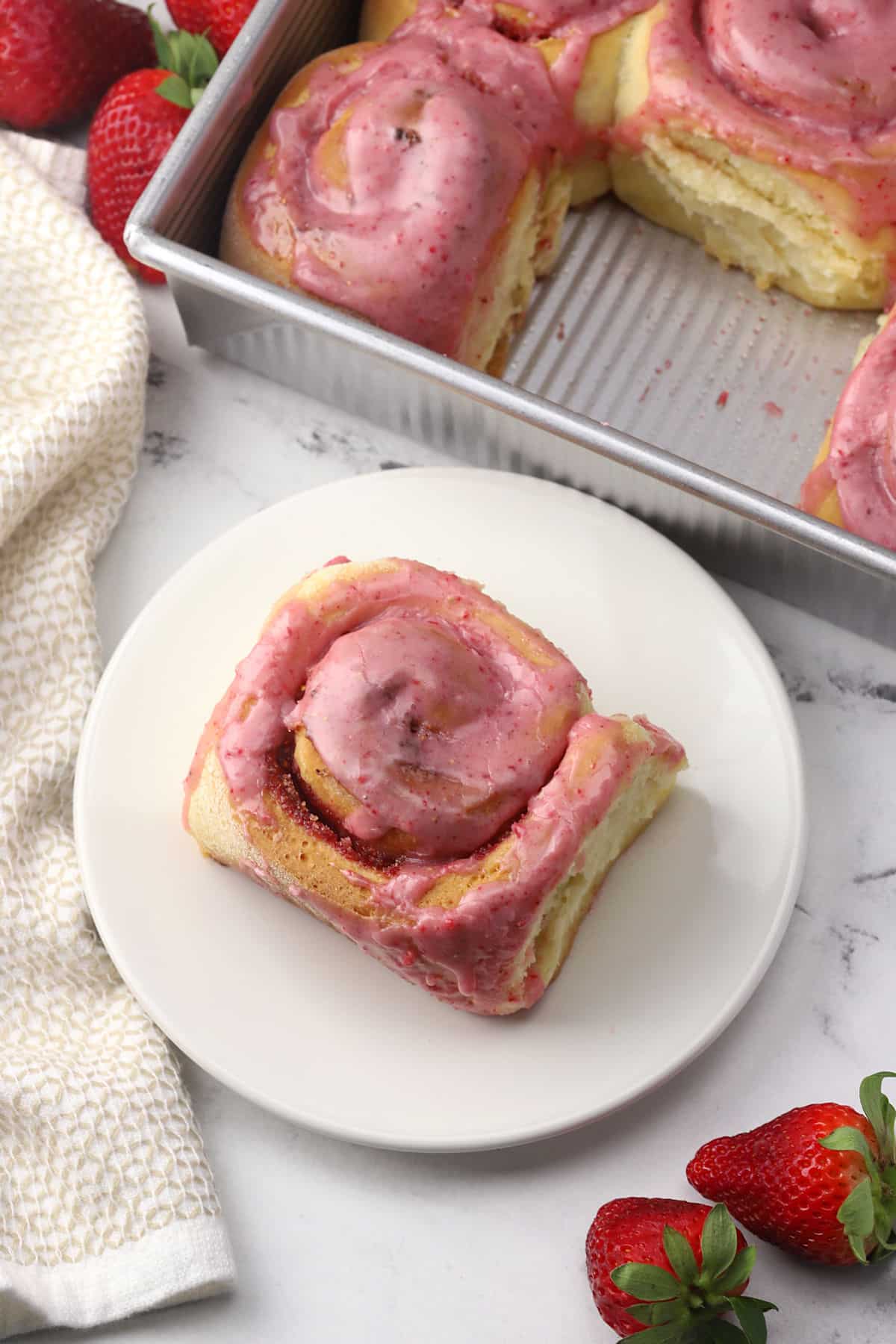 A sweet roll on a plate with a pan of more in the background.