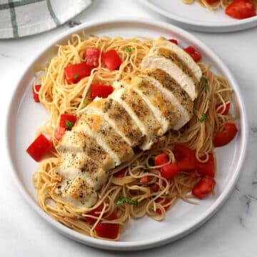 Two plates of pasta with sliced chicken breast laid on top.
