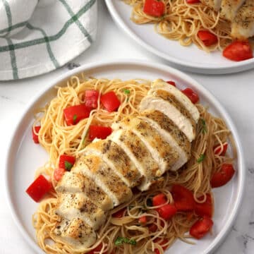 Two plates of pasta with sliced chicken breast laid on top.