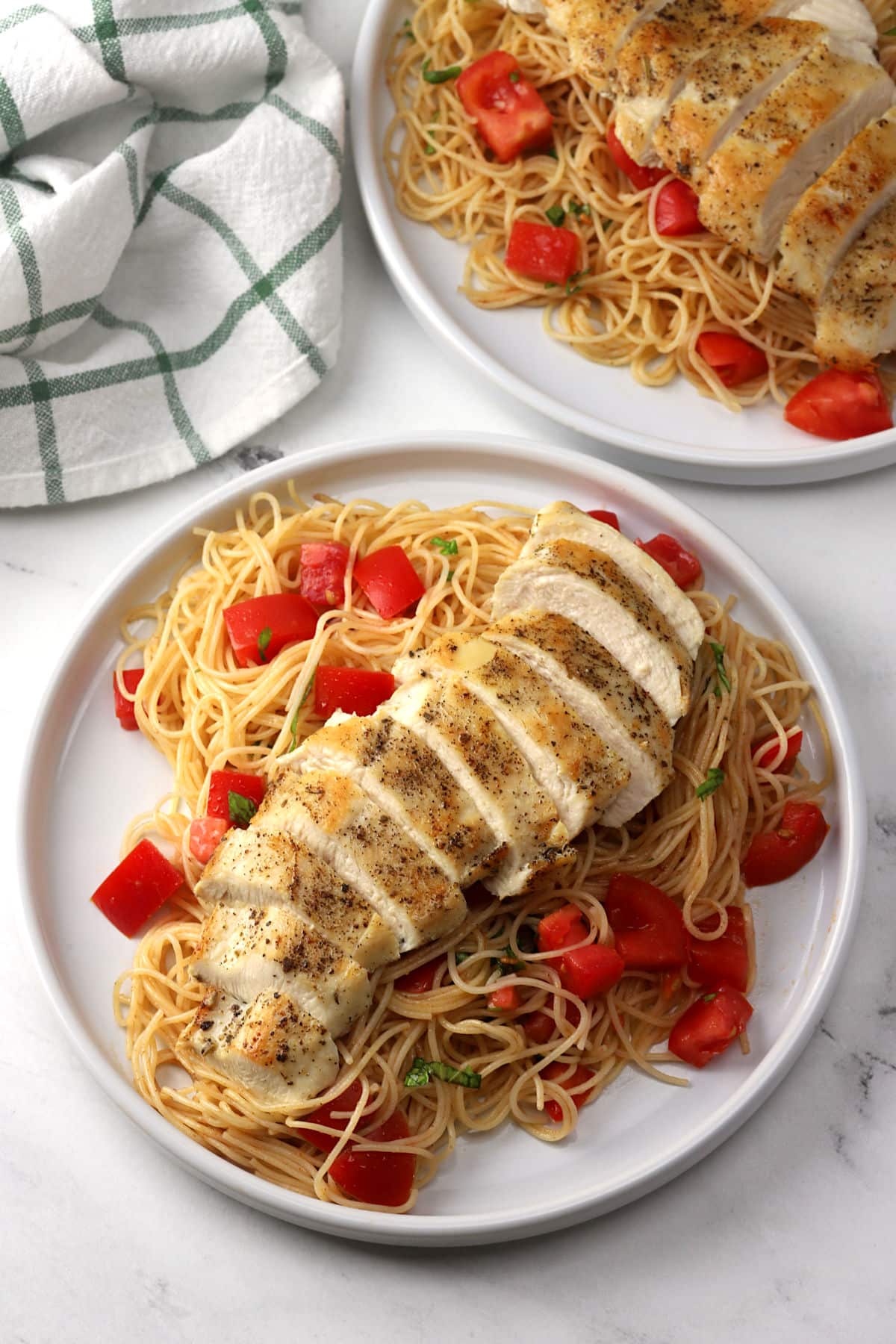 Two plates of pasta with sliced chicken breast laid on top.