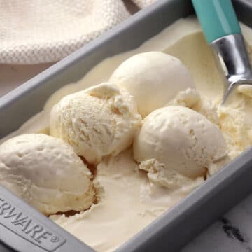 A metal pan of vanilla ice cream with an ice cream scooper.