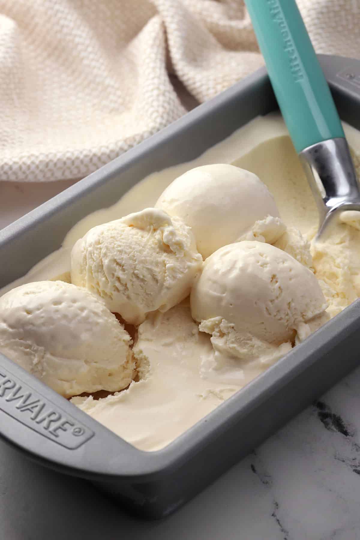 A metal pan of vanilla ice cream with an ice cream scooper.