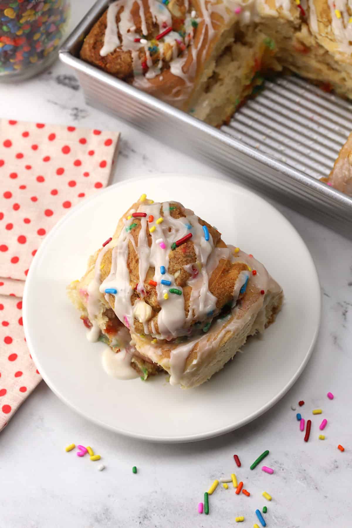 A cookie cinnamon roll on a plate with sprinkles.