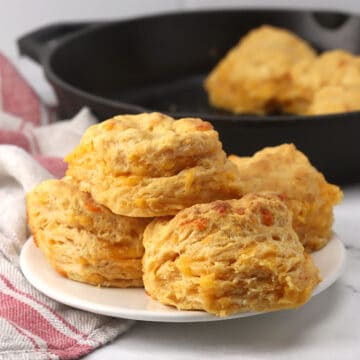 A plate of stacked biscuits with a cast iron skillet in the background.