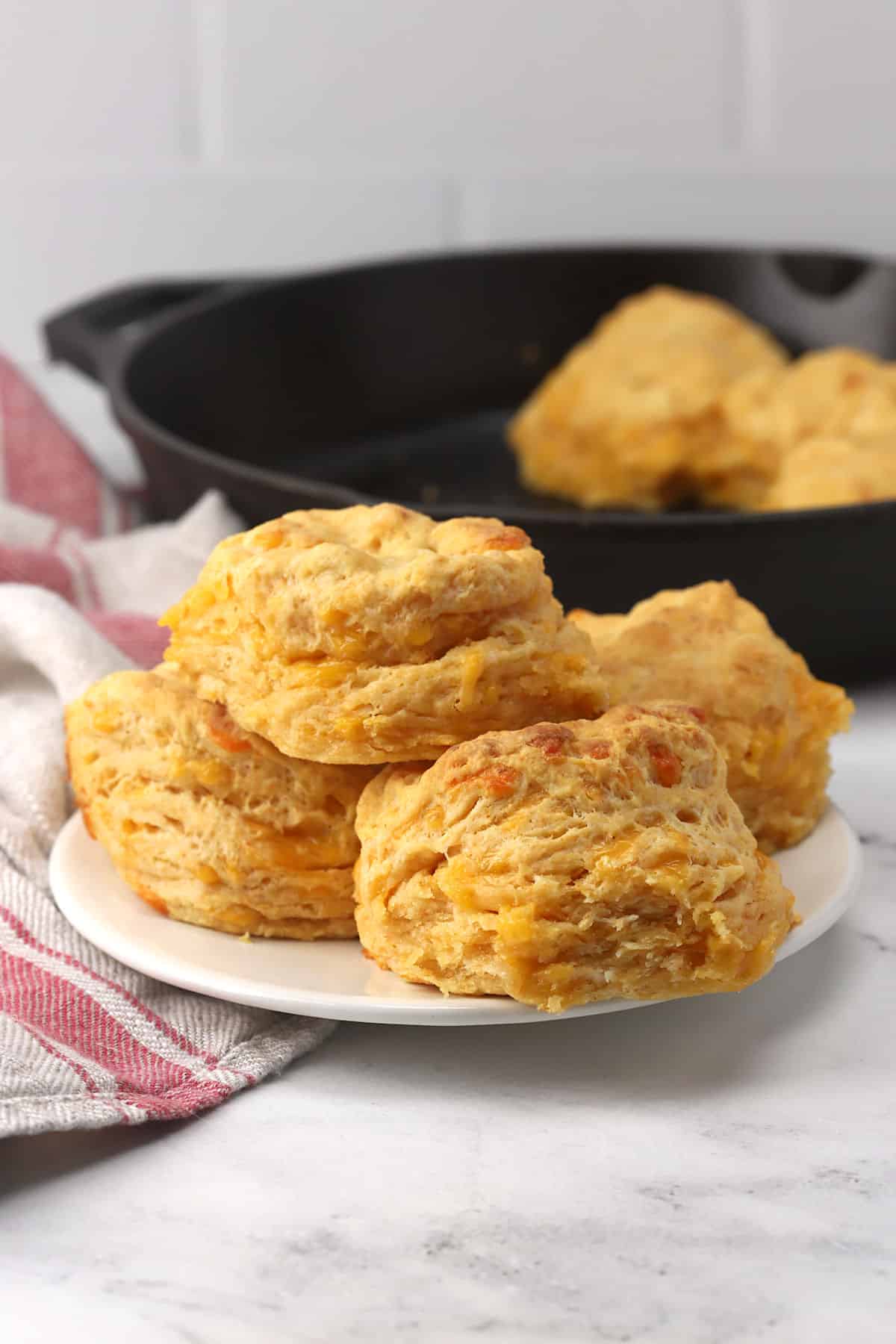 A plate of stacked biscuits with a cast iron skillet in the background.