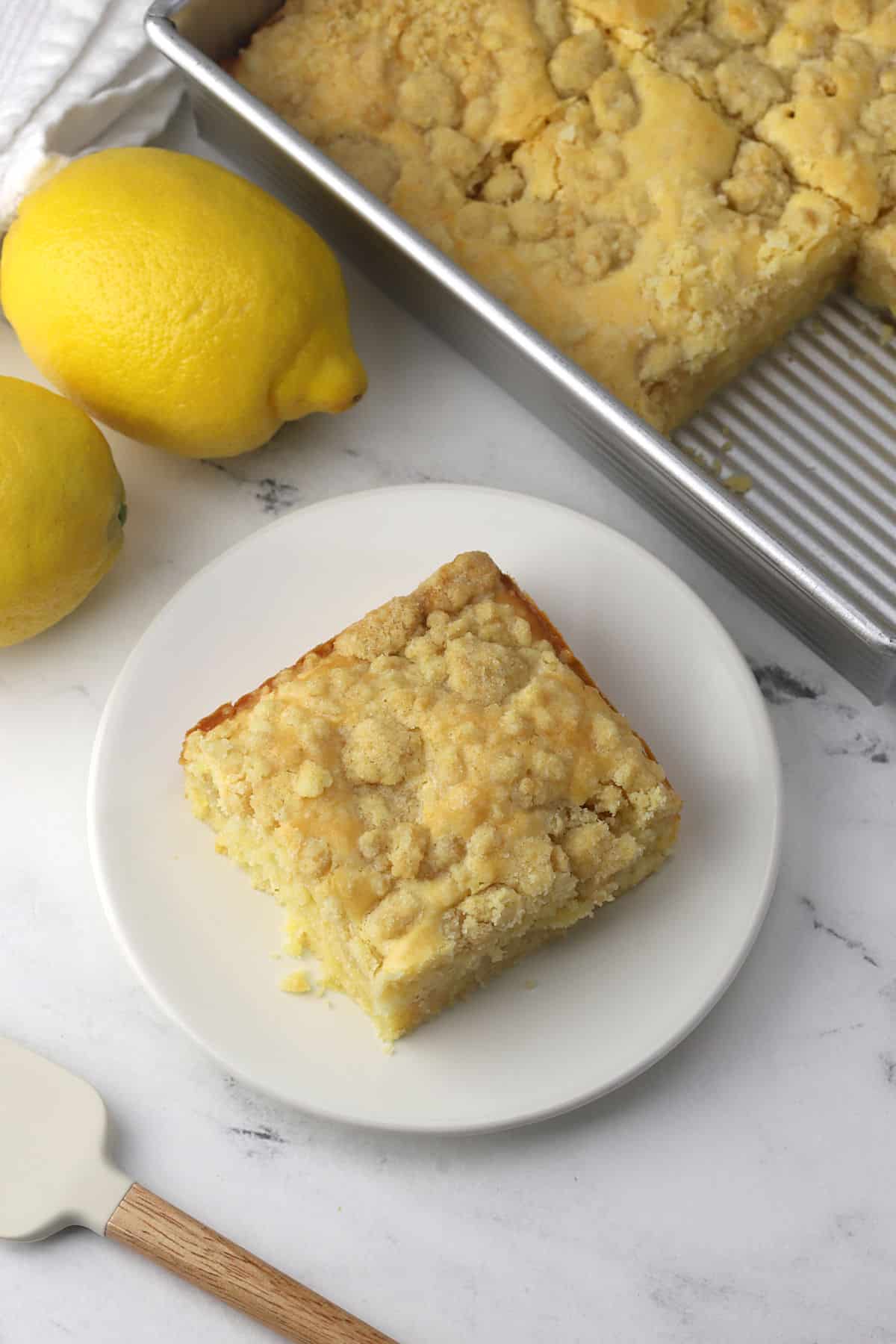 A slice of coffee cake on a plate with a lemon nearby.