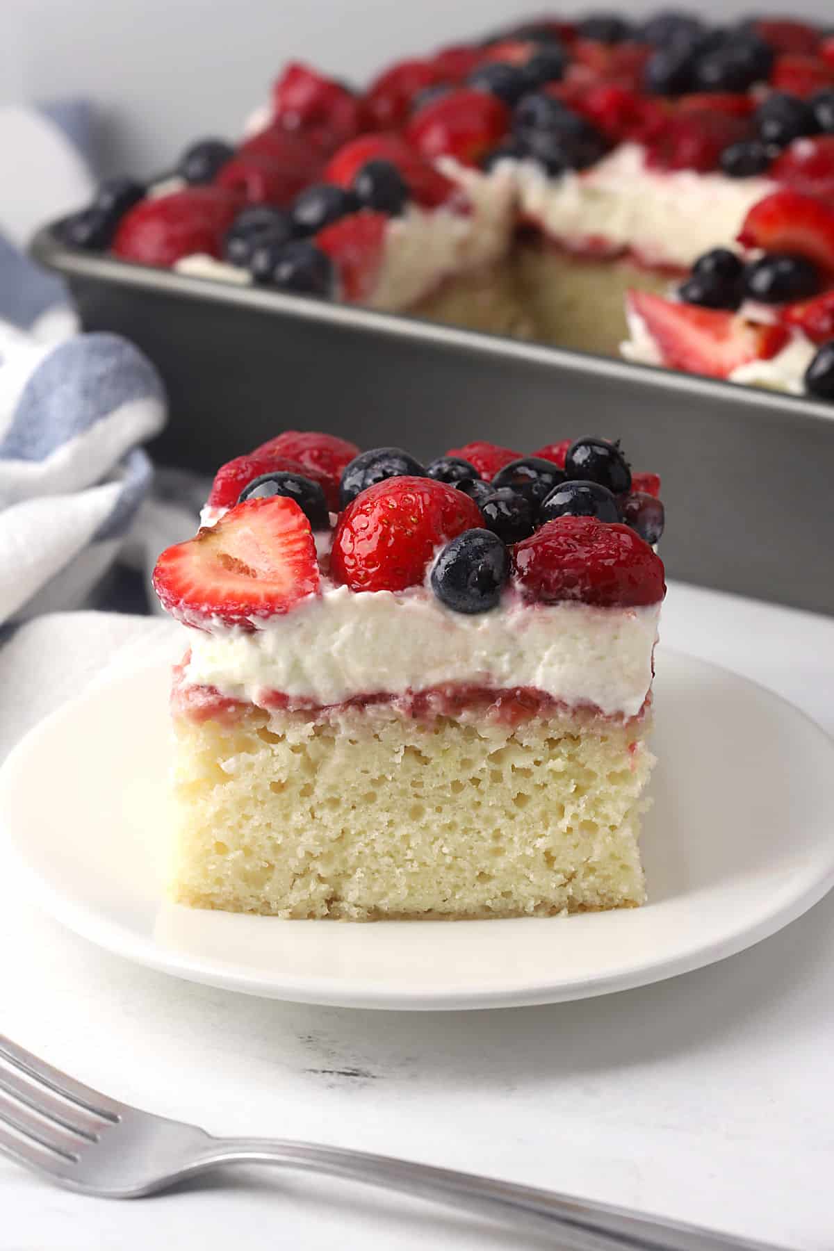 A slice of sheet cake with layered topping on a small plate with a fork.