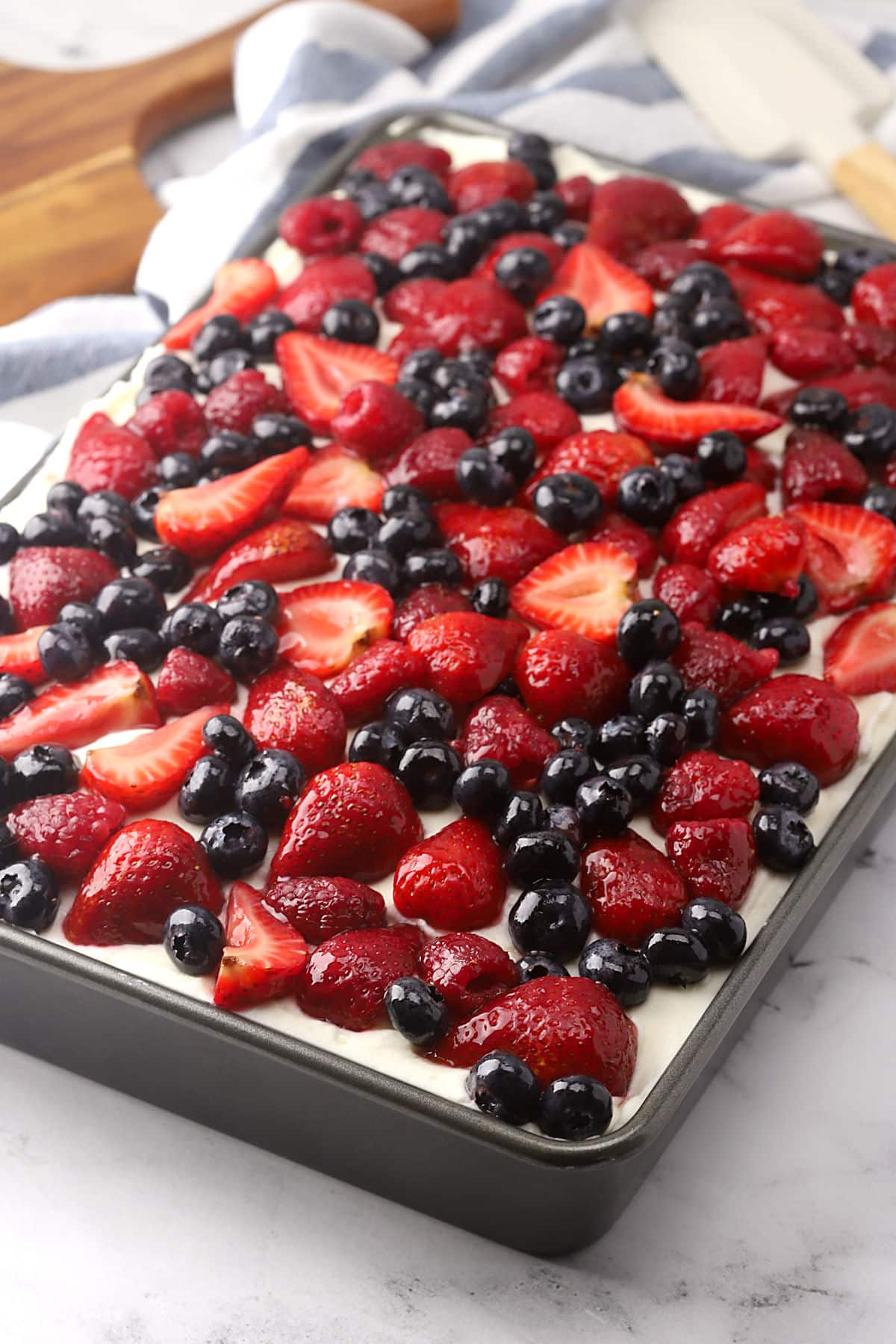 A cake pan of cake frosted and topped with glazed berries.