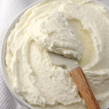A wooden spatula scooping frosting from a bowl.