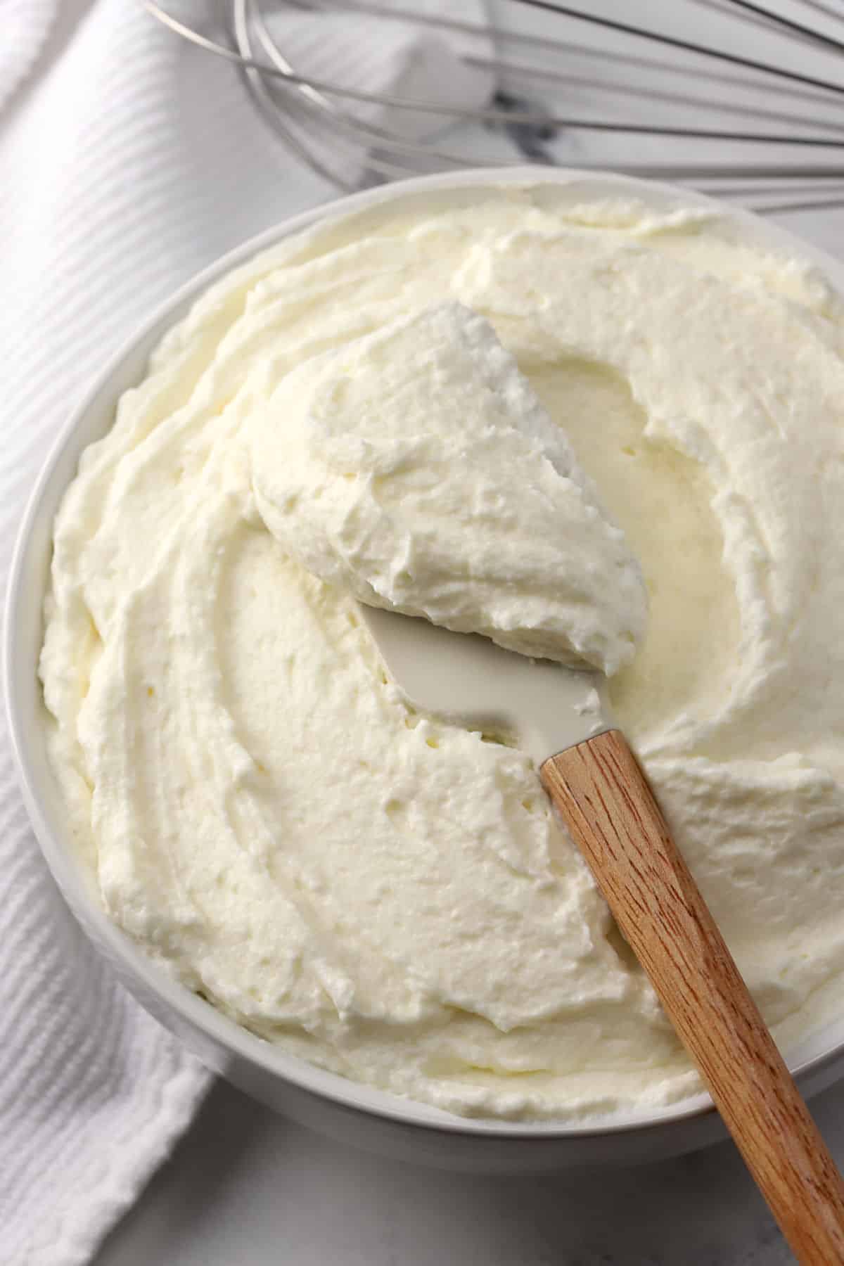 A wooden spatula scooping frosting from a bowl.