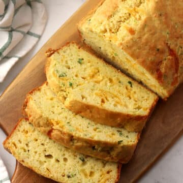 A loaf of cheddar garlic zucchini bread sliced on a wooden serving board.