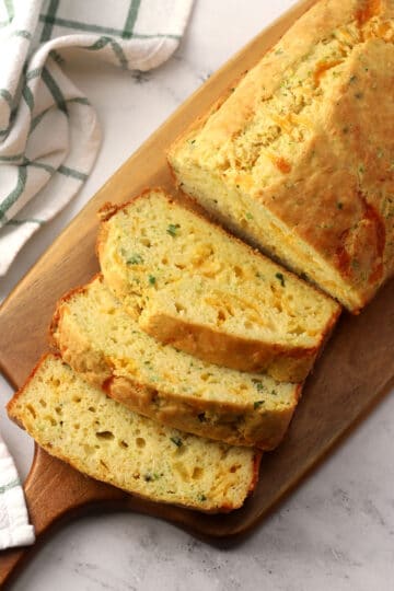 A loaf of cheddar garlic zucchini bread sliced on a wooden serving board.