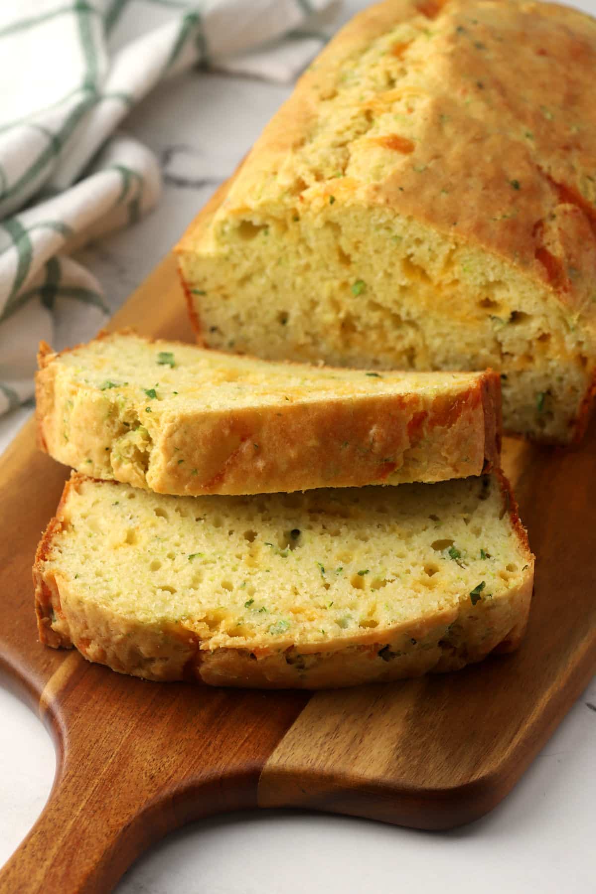 A close up view of two slices of cheddar garlic zucchini bread stacked on a serving board.