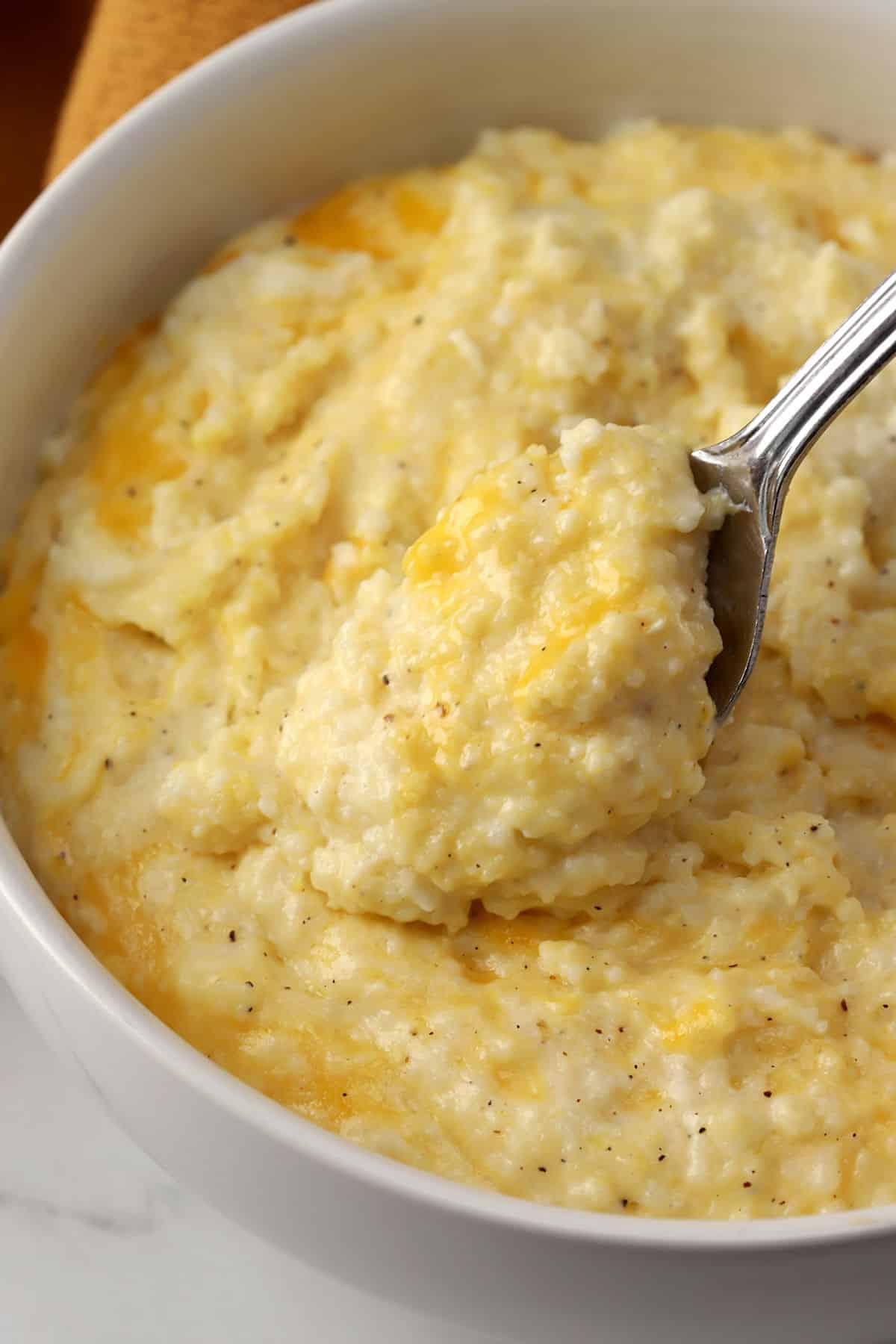 A spoon scooping cheesy grits from a bowl.